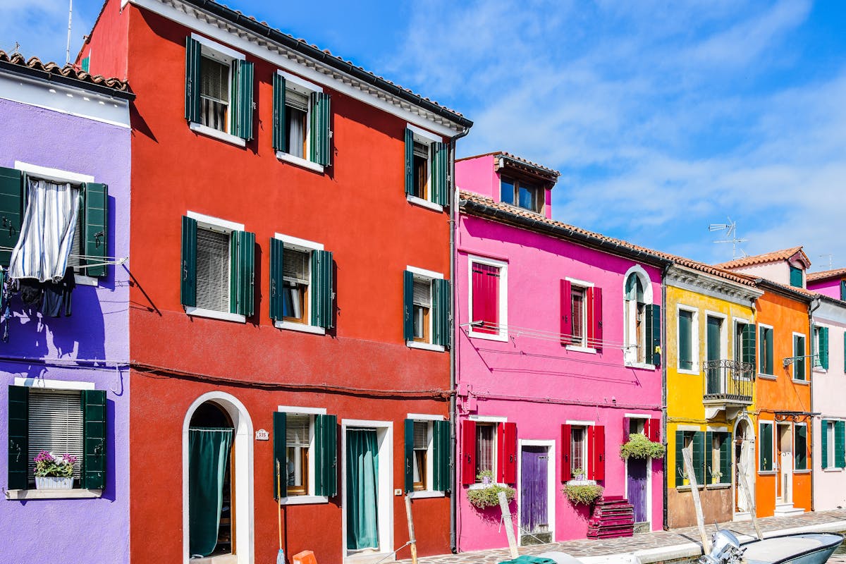 Row of brightly painted houses along a canal in Burano, each a different vivid colour